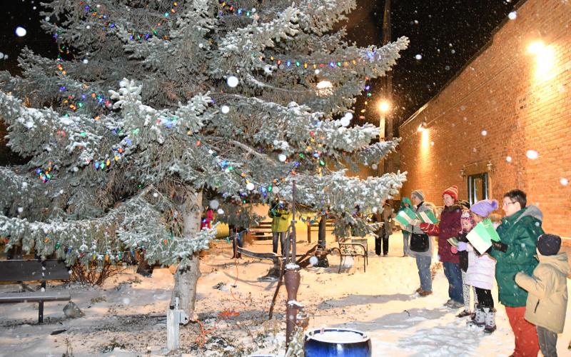 A group gathers around the large evergreen tree in the center of the Day County Arts Council’s mural garden and sings Christmas carols just moments after the official first lighting of the tree Dec. 1. From right are Ronan Smidt, Tandra Smidt, Amara Pool, Aly Moos, Jennifer Moos and Sandra Rood. Reporter &amp;amp; Farmer | Amanda Dulitz