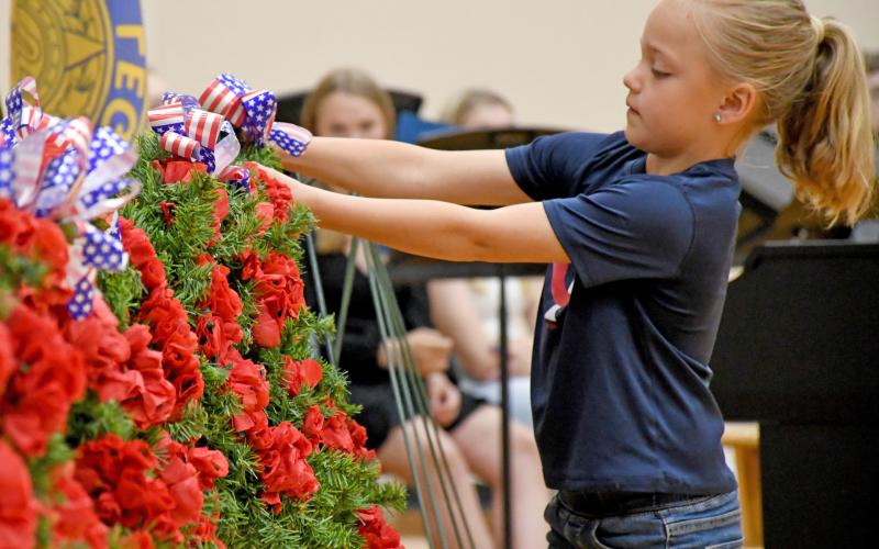 Webster Junior American Legion Auxiliary member Elsie Zubke hangs a wreath during the Webster Memorial Day program May 26 at Webster Area High School gym. Members of the youth oriented veteran support organization took turns hanging a wreath, each representing a different war time era and effort. Reporter &amp;amp; Farmer | Amanda Dulitz