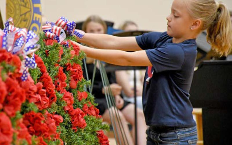 Webster Junior American Legion Auxiliary member Elsie Zubke hangs a wreath during the Webster Memorial Day program May 26 at the Webster Area High School gym. Members of the youth oriented veteran support organization took turns hanging a wreath – each one representing a different war time era and effort. Reporter &amp;amp; Farmer | Amanda Dulitz