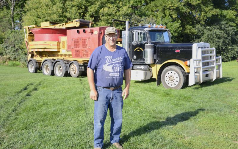 Mike Meland, owner/operator of Meland Haygrinding LLC, stands in his farmyard in southern Day County with one of his truck-mounted hay grinders seen in the background. Meland has been running the business since 2006 with the help of his wife Jennifer and their four kids.