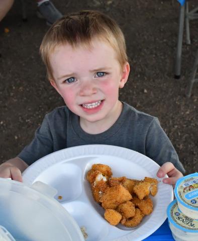 Nolan Andrews cheeses with his plate of fish at the grand opening of the Glacial Lakes Fish Cleaning Station in Webster. January 2024 the City of Webster approved to move forward with the station. Webster Area Chamber of Commerce president Katy Marx who has worked closely with the project stated, “The event turned out great. The support was amazing.” Reporter &amp; Farmer | Annie Witt