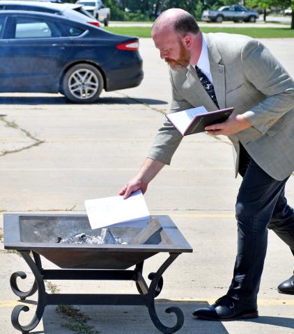 Reverend Dr. Jason Holt, a Presidential Ministry Associate with American Free Lutheran Church Congregations, places the paid off mortgage paperwork for Tabor Lutheran Church in Webster in a fire pit during a mortgage burning ceremony July 14. The church purchased what was formerly Shopko along U.S. Hwy. 12 in Webster and converted it to their worship center, paying down the 20-year loan in four and a half years, to the day. Reporter &amp; Farmer | Amanda Dulitz
