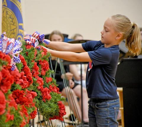 Webster Junior American Legion Auxiliary member Elsie Zubke hangs a wreath during the Webster Memorial Day program May 26 at Webster Area High School gym. Members of the youth oriented veteran support organization took turns hanging a wreath, each representing a different war time era and effort. Reporter &amp; Farmer | Amanda Dulitz