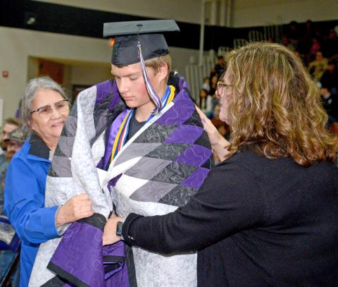 At Waubay High School’s graduation, certain members of the class of 2025 received star quilts to celebrate their accomplishments. Here, Sandi Bernard helps wrap a quilt around graduate Dylan Rumpza while his mom Deb Rumpza also helps wrap the fabric around his shoulders. Waubay saw 12 seniors cross the stage and turn their tassels May 17 at Waubay High School gym. Rumpza was the class salutatorian. Reporter &amp; Farmer | Amanda Dulitz