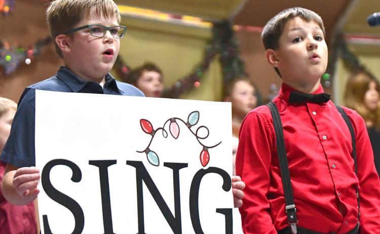 Webster Area third grade students, from left, Rhiley Zimmerman and Archer Chevalier sing during the school’s elementary winter concert Dec. 8 at the Webster Armory. Reporter &amp; Farmer | Leyton Beardslee
