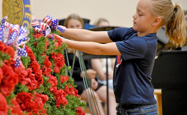 Webster Junior American Legion Auxiliary member Elsie Zubke hangs a wreath during the Webster Memorial Day program May 26 at Webster Area High School gym. Members of the youth oriented veteran support organization took turns hanging a wreath, each representing a different war time era and effort. Reporter &amp; Farmer | Amanda Dulitz