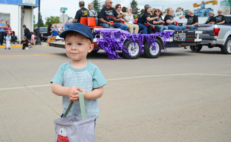 Two-year-old Boone Lesnar smiles after gathering a handful of candy tossed out by members of a Webster High School alumni class float June 27 for the alumni parade. He and many other children in town for the event were beneficiaries of the sweet treats class members tossed to onlookers. Lesnar is the son of Mike and Amber Lesnar of rural Webster. Reporter &amp; Farmer | Amanda Dulitz