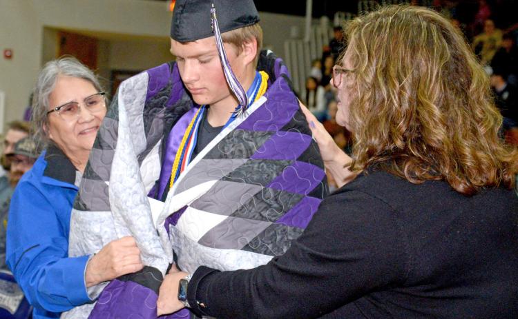At Waubay High School’s graduation, certain members of the class of 2025 received star quilts to celebrate their accomplishments. Here, Sandi Bernard helps wrap a quilt around graduate Dylan Rumpza while his mom Deb Rumpza also helps wrap the fabric around his shoulders. Waubay saw 12 seniors cross the stage and turn their tassels May 17 at Waubay High School gym. Rumpza was the class salutatorian. Reporter &amp; Farmer | Amanda Dulitz